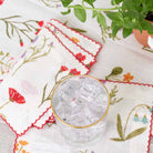 Red poppy flowers, mini yellow daffodils, and lavender bluebells on a soft white linen base.