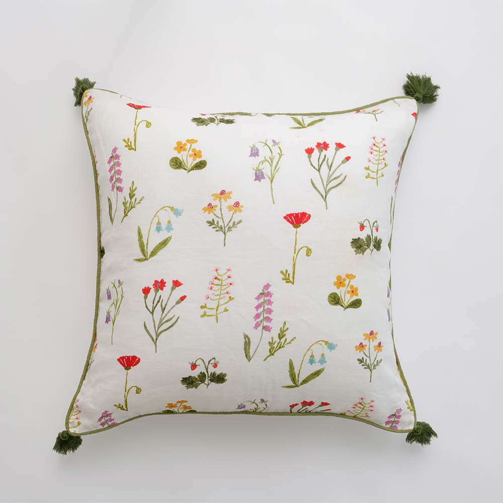 Throw pillow cover with red poppy flowers, mini yellow daffodils, and lavender bluebells on a soft white linen base with green border stitching and pom poms.