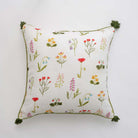 Throw pillow cover with red poppy flowers, mini yellow daffodils, and lavender bluebells on a soft white linen base with green border stitching and pom poms.