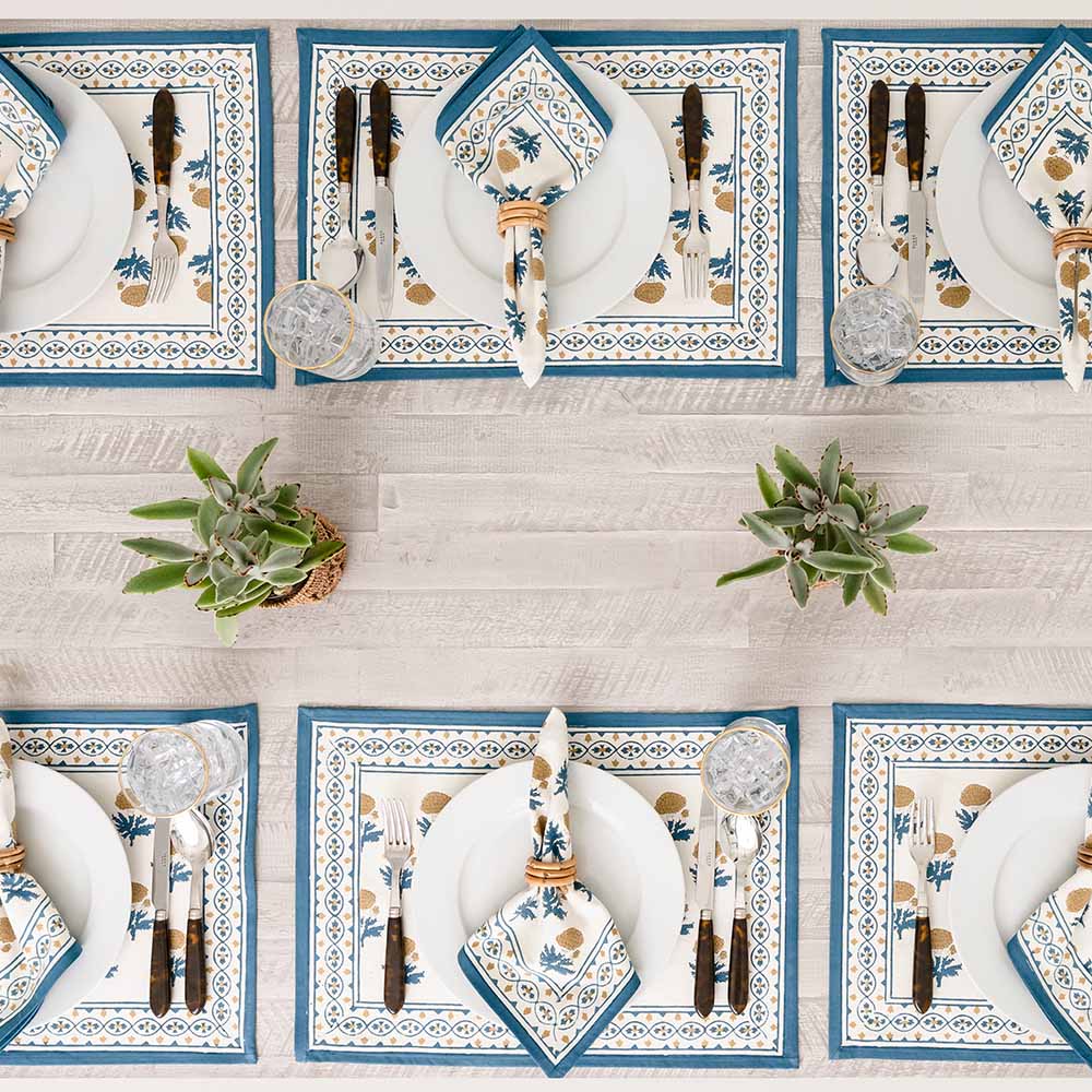 Dinner table with matching placemats and napkins with plants as centerpieces. 