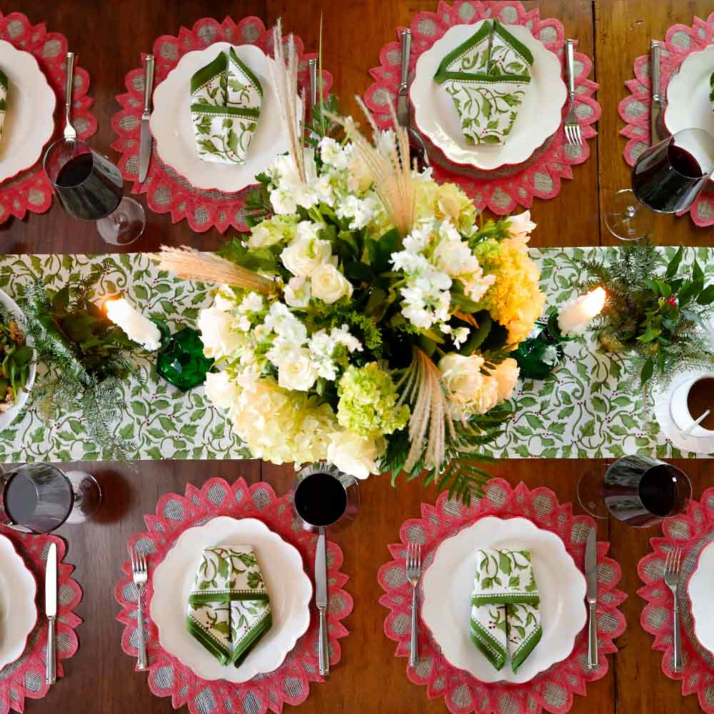 A table runner with a holly berry design on a wooden table with a dinner table setting