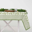 A set table covered with a green and white tablecloth featuring a holly berry pattern, arranged with dishes and silverware.