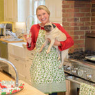 Model wearing Holly Berry green and white apron holding a glass of wine and a dog