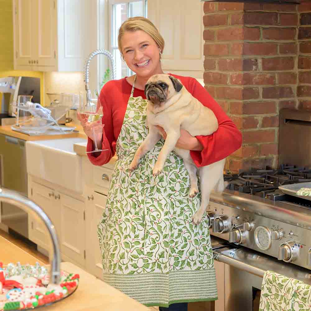 Model wearing Holly Berry green and white apron holding a glass of wine and a dog