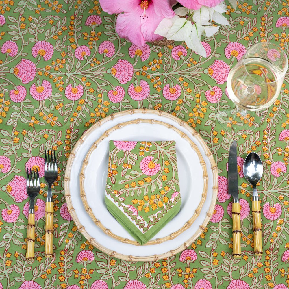 A set of cloth napkins with a floral pattern, predominantly pink and green, displayed on a table setting with dishes and cutlery.