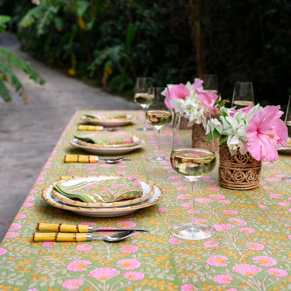 A tablecloth with a floral pattern featuring pink flowers and green leaves displayed on a table outdoors.