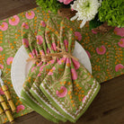 A set of cloth napkins with a floral pattern in pink, green, and yellow, displayed on a white plate with a matching table runner.