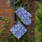 Pomegranate Blue oven mitt and potholder set with greenery in the background.