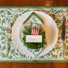 A set of four cotton placemats with a Christmas holly and berries pattern displayed on a table setting alongside a plate and cutlery.